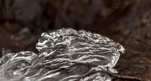 A piece of ice frozen on a tree branch close-up against the dark water of a fast river in early winter