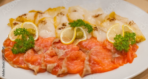 Sliced red salmon and white oily fish decorated with lemon wedges, dill sprigs and green olives on a white ceramic plate close-up