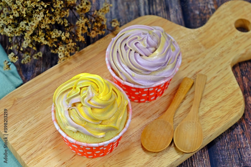 Homemade cupcakes served on wooden cutting board with wooden spoons on wooden table.