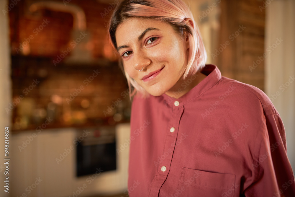 Stylish cool teenage girl with no make up, pinkish bob hairdo and ring in her nose posing indoors, relaxing at home, having carefree happy look. Beauty, style, fashion and self-expression concept Stylish cool teenage girl with no make up, pinkish bob hairdo and ring in her nose posing indoors, relaxing at home, having carefree happy look. Beauty, style, fashion and self-expression concept
