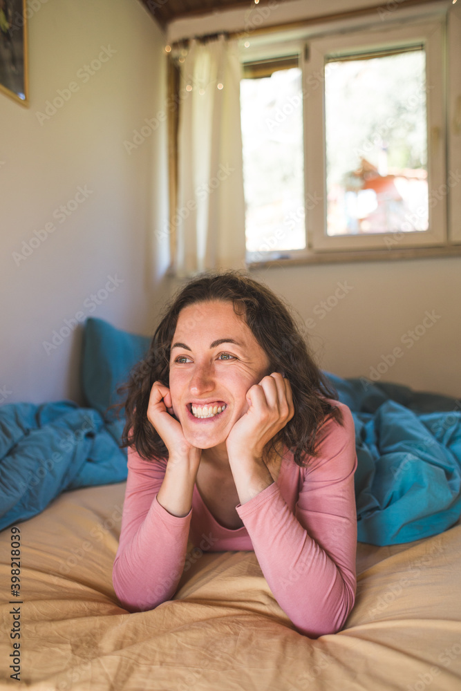 A smiling woman of thirty lies in bed after waking up. A smiling woman of thirty lies in bed after waking up.