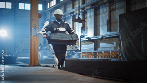 Black African American Engineer is Testing a Futuristic Bionic Exoskeleton and Proudly Wearing it in a Heavy Steel Industry Factory. Powered Mobile Machine Shell made for Helping Workers.