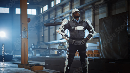 Black African American Engineer is Testing a Futuristic Bionic Exoskeleton and Proudly Posing in Heavy Steel Industry Factory. Powered Mobile Machine Shell made for Helping Workers.