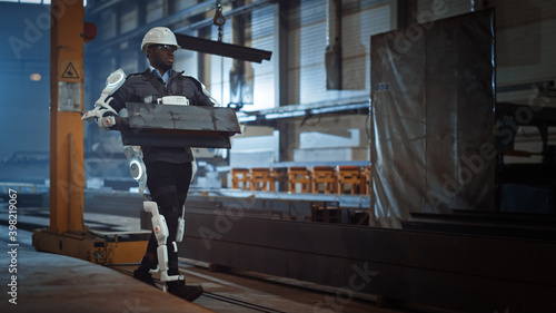 Black African American Engineer is Testing a Futuristic Bionic Exoskeleton and Proudly Wearing it in a Heavy Steel Industry Factory. Powered Mobile Machine Shell made for Helping Workers.