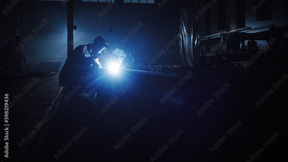 Heavy Industry Engineering Factory Interior with Industrial Worker Using a Welding Machine and Working on a Metal Tube. Contractor in Safety Uniform and Hard Hat Manufacturing Metal Structures.