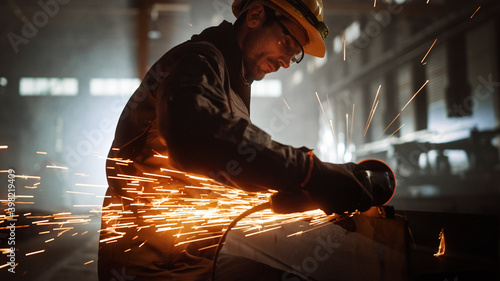 Fotografia Heavy Industry Engineering Factory Interior with Industrial Worker Using Angle Grinder and Cutting a Metal Tube