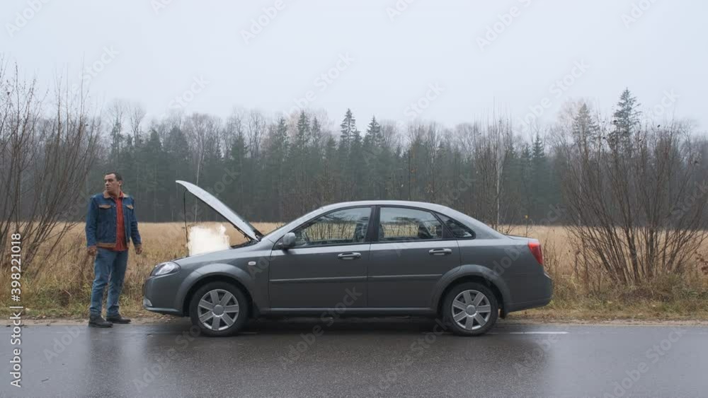 Sad man standing on the road by the broken car. Smoke coming out the engine. Help needed. Car service. Tow service. Sad man standing on the road by the broken car. Smoke coming out the engine. Help needed. Car service. Tow service.