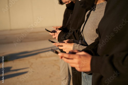 Hands of a group of friends using a smart phone. They are dressed in black and gray, without any color in the scene. © CarlosBarquero
