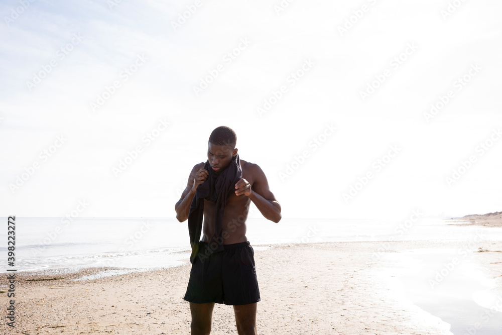 Young black sportsman on the beach who wears the sport shirt, young man who wears sport shorts.
