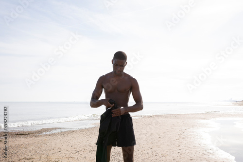 Young black athlete on the beach getting ready to wear the sports shirt.