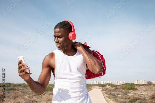 Shot of young black athlete smiles while listening to music on his mobile with red headphones. Young man laughing while chatting.