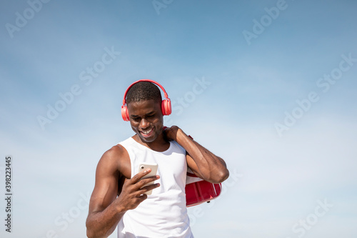 Young black sportsman laughing while listening to music on his cell phone. Young man laughing while chatting. © menudencias