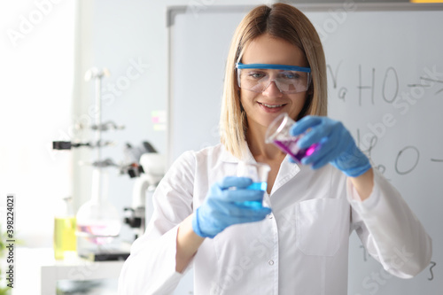 Woman scientist in safety glasses pouring chemical solution from flask in laboratory