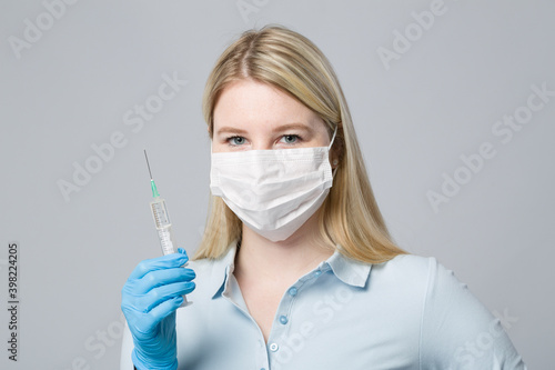 female doctor or nurse with medical face mask and medical gloves with a pulled up syringe ready for vaccination 