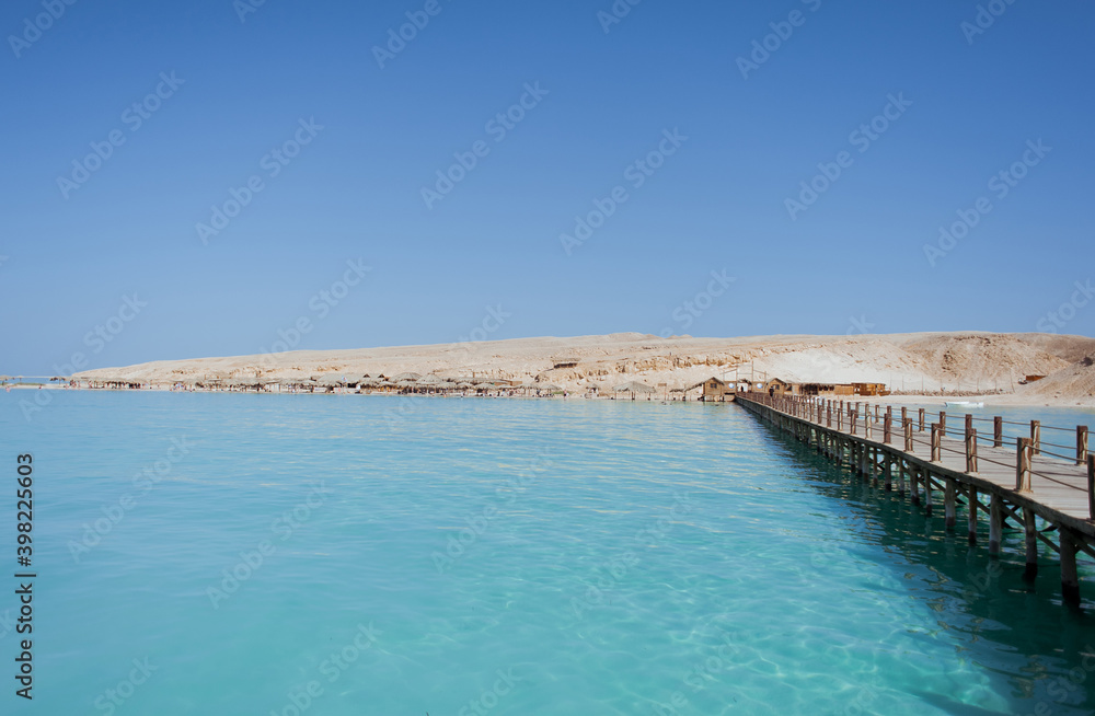 A bridge leading to a sandy island. Around the blue sea water. Summer. Heat. Egypt.