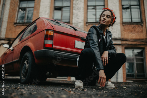 Young woman sits on street near red retro car.
