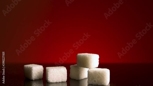 Light shines on stack of sugar cubes that lying on dark table surface isolated on red background. Stock footage. Close up of white sugar, concept of food and cooking.  photo