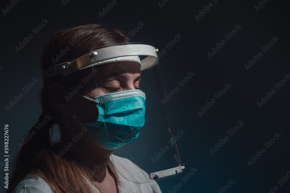 female doctor with face shield and mask, closed eyes, side view on dark background female doctor with face shield and mask, closed eyes, side view on dark background
