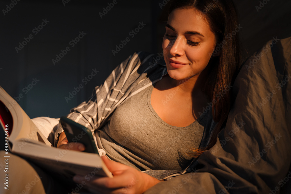 Charming happy woman using mobile phone and reading book in bed Charming happy woman using mobile phone and reading book in bed