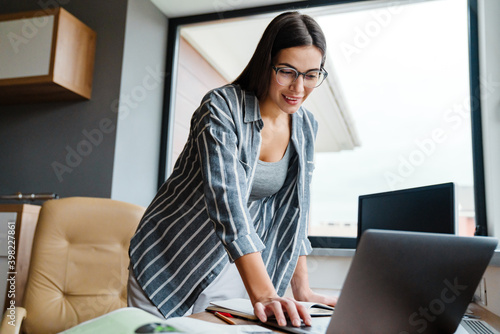 Charming cheerful woman working with laptop while standing at table