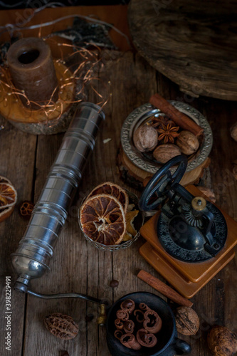 Cinnamon sticks, dried orange, star anise, aromatic spices on a wooden table. Christmas lights garlands. New Year's still life. Manual coffee grinder and beans. Food on the table.