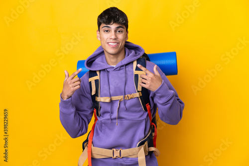 Young mountaineer man with a big backpack over isolated yellow background giving a thumbs up gesture