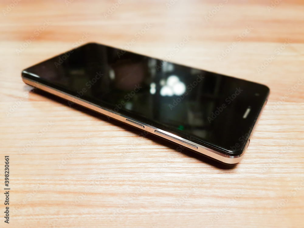 Black modern smartphone with blank screen on wooden surface. Selective focus. Black modern smartphone with blank screen on wooden surface. Selective focus.