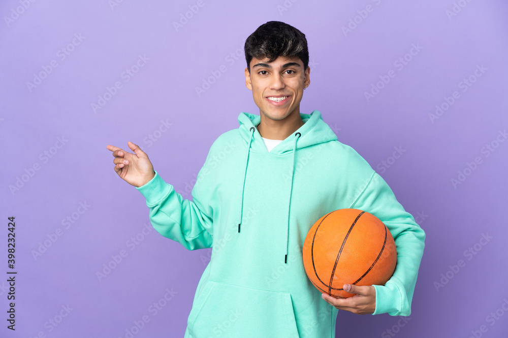 Young man playing basketball over isolated purple background pointing finger to the side