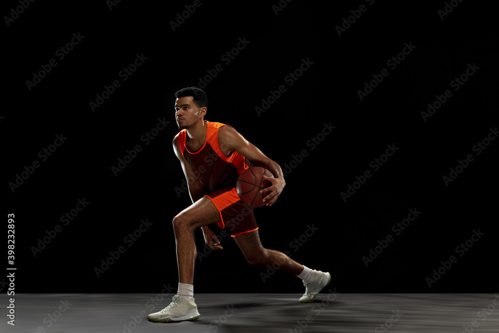 Leader. Young purposeful african-amrican basketball player training, practicing in action, motion isolated on black background. Concept of sport, movement, energy and dynamic, healthy lifestyle.