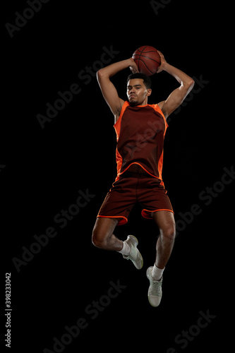 High. Young purposeful african-amrican basketball player training, practicing in action, motion isolated on black background. Concept of sport, movement, energy and dynamic, healthy lifestyle.