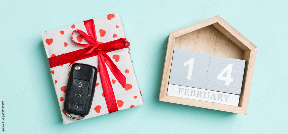 Obraz premium Top view of car key on a gift box with red hearts and festive calendar on colorful background. The fourteenth of february. Present for Valentine's Day concept