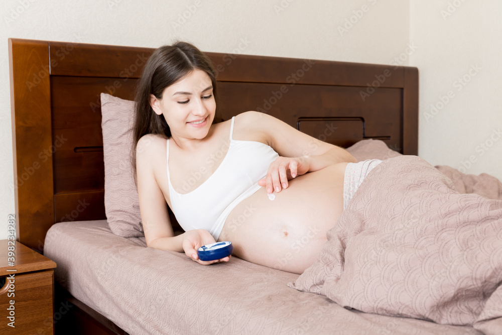 pregnant woman applying stretch mark cream to belly. pregnancy, people and maternity concept. pregnant apply anti-stretch mark cream on her belly