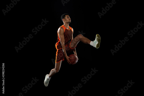 Overcome. Young purposeful african-amrican basketball player training, practicing in action, motion isolated on black background. Concept of sport, movement, energy and dynamic, healthy lifestyle.