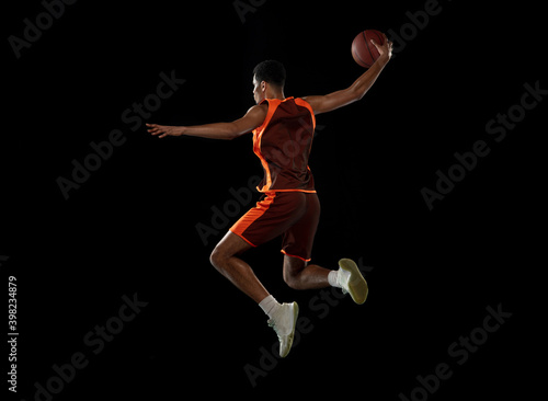 Flying. Young purposeful african-amrican basketball player training, practicing in action, motion isolated on black background. Concept of sport, movement, energy and dynamic, healthy lifestyle. © master1305