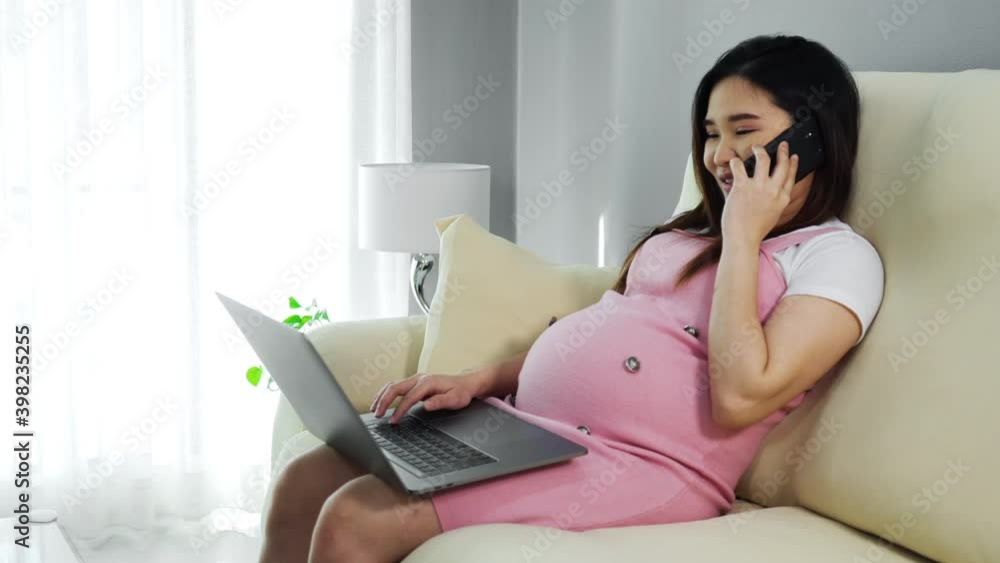 pregnant woman using smartphone and laptop computer on sofa in the living room pregnant woman using smartphone and laptop computer on sofa in the living room