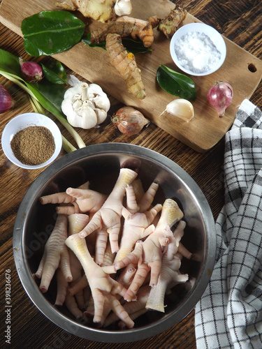 Raw chicken claws or ceker or cakar ayam in frame with herbs and spices to season it, such as coriander, ginger, turmeric, lemon grass, lime leaves. Typical Indonesian food. Cooking preparation. photo