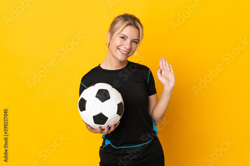 Young Russian football player woman isolated on yellow background saluting with hand with happy expression © luismolinero