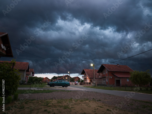 Stormy severe weather during storm with dark scary clouds, above settlement during summer evening.