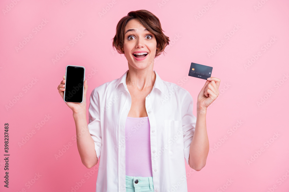 Photo of surprised charming young lady wear white shirt holding modern device bank card isolated pastel pink color background Photo of surprised charming young lady wear white shirt holding modern device bank card isolated pastel pink color background