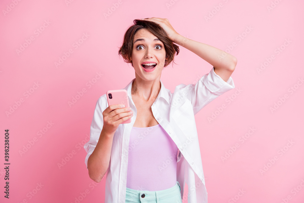 Photo of cheerful amazed girl hold hand head phone notification reaction wear white shirt isolated on pink color background Photo of cheerful amazed girl hold hand head phone notification reaction wear white shirt isolated on pink color background