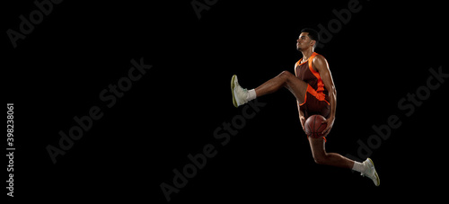 Flying. Young purposeful african-amrican basketball player training, practicing in action, motion isolated on black background. Concept of sport, movement, energy and dynamic, healthy lifestyle. © master1305