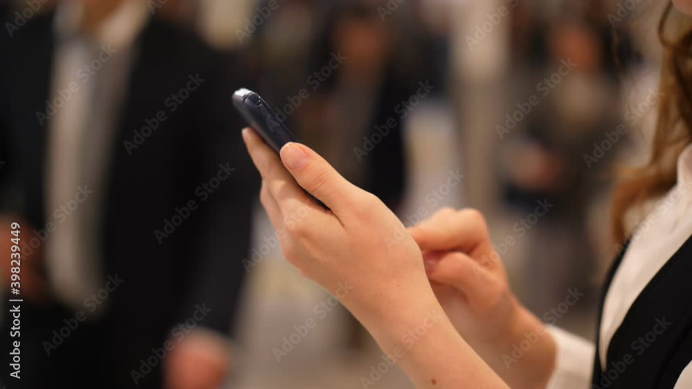 Woman using phone, close up shot of hands and mobile device. Blurred background, many people walk at Osaka metro station passage, evening time rush Woman using phone, close up shot of hands and mobile device. Blurred background, many people walk at Osaka metro station passage, evening time rush