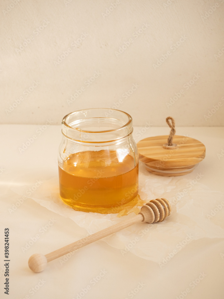 Glass jar with acacia honey and a wooden spoon for honey on a light background in the morning light Glass jar with acacia honey and a wooden spoon for honey on a light background in the morning light