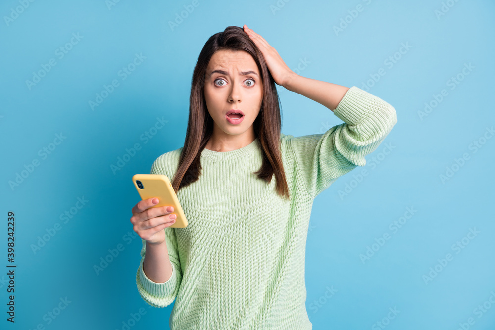 Photo portrait of upset woman touching head with one hand holding phone isolated on pastel blue colored background Photo portrait of upset woman touching head with one hand holding phone isolated on pastel blue colored background