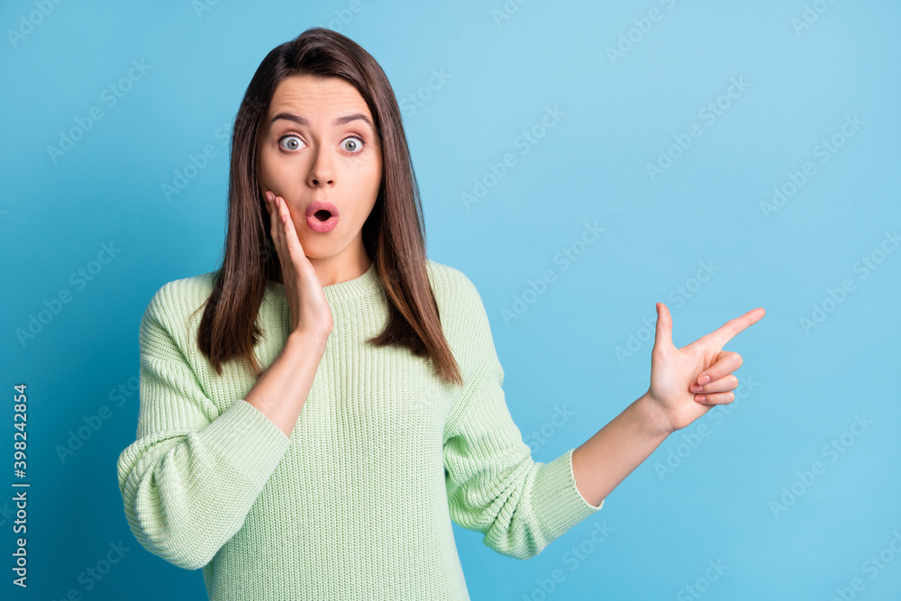 Photo of lovely young girl indicate finger empty space crazy face open mouth wear green pullover isolated blue color background Photo of lovely young girl indicate finger empty space crazy face open mouth wear green pullover isolated blue color background