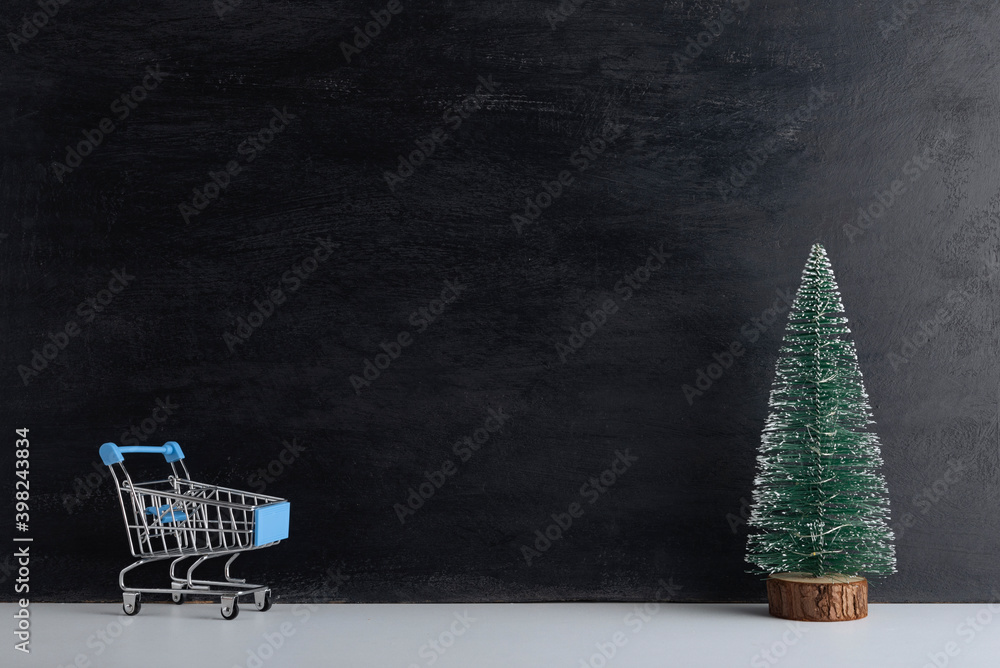 Shopping cart and miniature Christmas tree on black background. New year shopping. Copy space