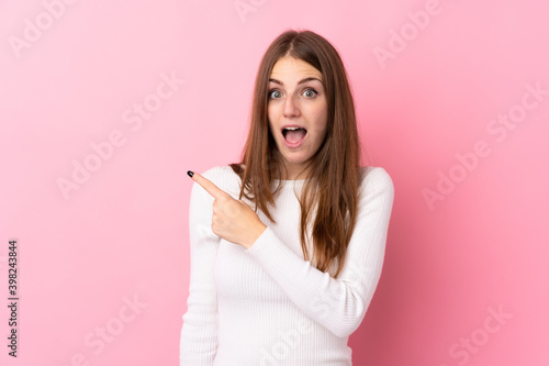 Young woman over isolated pink background surprised and pointing side