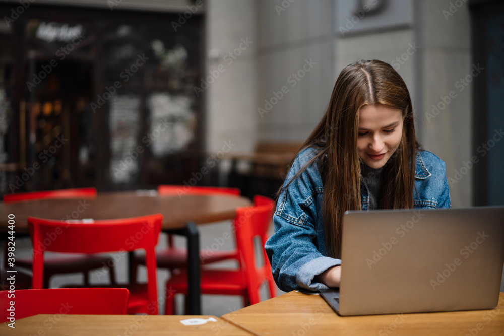 Beautiful happy girl working with laptop while sitting in street cafe Beautiful happy girl working with laptop while sitting in street cafe
