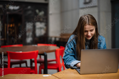 Beautiful happy girl working with laptop while sitting in street cafe