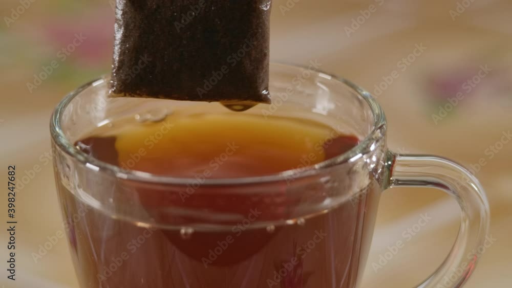 Slow Motion Close Up Glass Cup With Black Tea Bag. Making Morning Tea. Putting Tea Bag Into Glass Cup Full of Hot Water Slow Motion Closeup. Slow Motion Close Up Glass Cup With Black Tea Bag. Making Morning Tea. Putting Tea Bag Into Glass Cup Full of Hot Water Slow Motion Closeup.